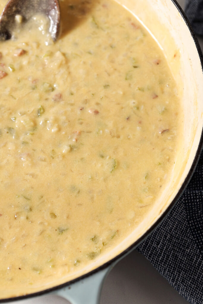 The cheesy sauce in a pan with a wooden spoon