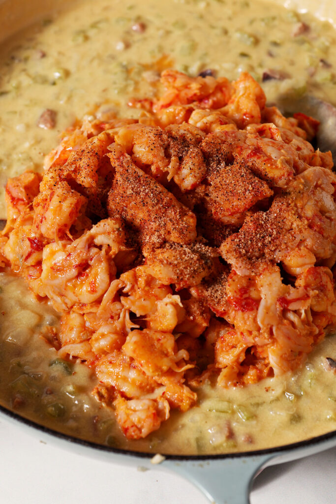 Crawfish tails and seasoning sit on top of a creamy sauce with vegetables in a pan