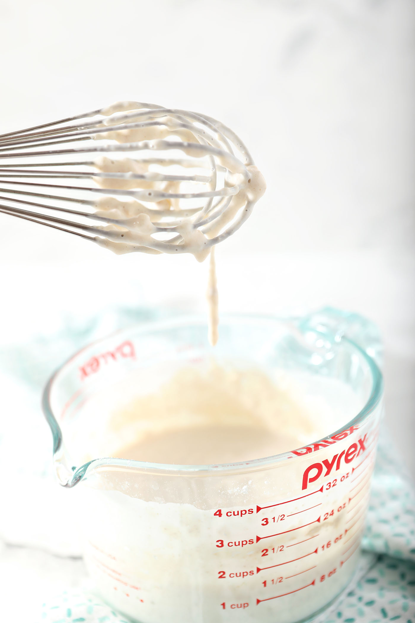 A whisk lifts out of a runny mixture, known as the sponge, in a liquid measuring cup