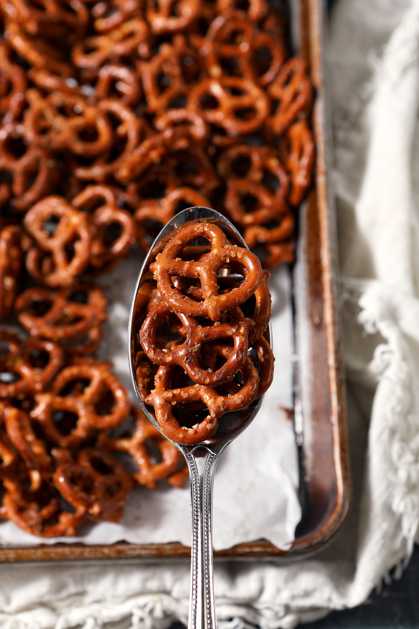 A spoon holds a few ranch pretzels above a sheet pan of just-baked ranch flavored pretzels