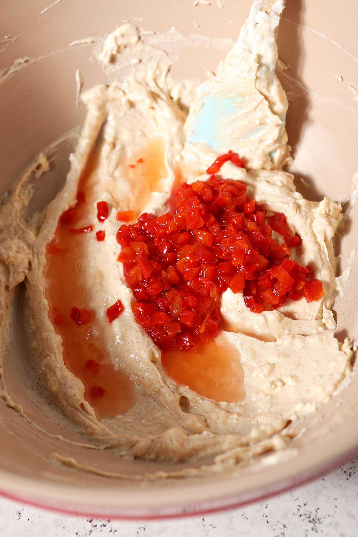 Diced pimentos and their juice on top of the creamy base mixture for pimento cheese in a bowl