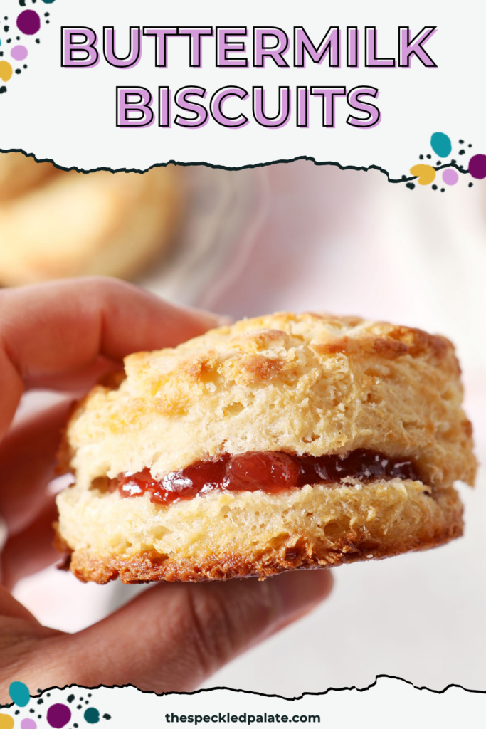 A hand holds a buttery biscuit filled with jam above a surface with more biscuits with the text buttermilk biscuits