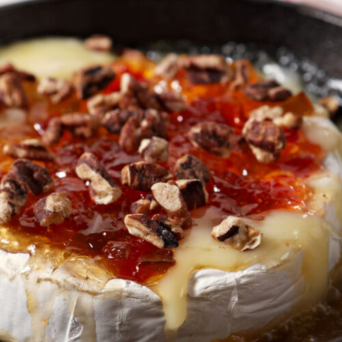 Close up of melty Baked Brie with Pepper Jelly and Toasted Pecans in a cast iron skillet
