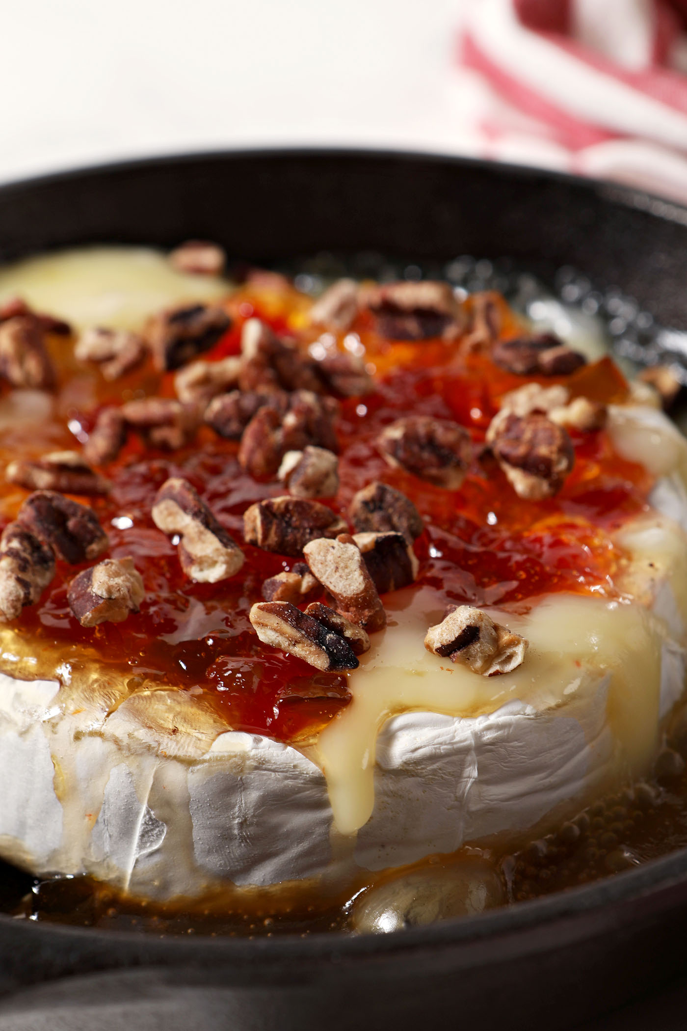 Close up of melty Baked Brie with Pepper Jelly and Toasted Pecans in a cast iron skillet