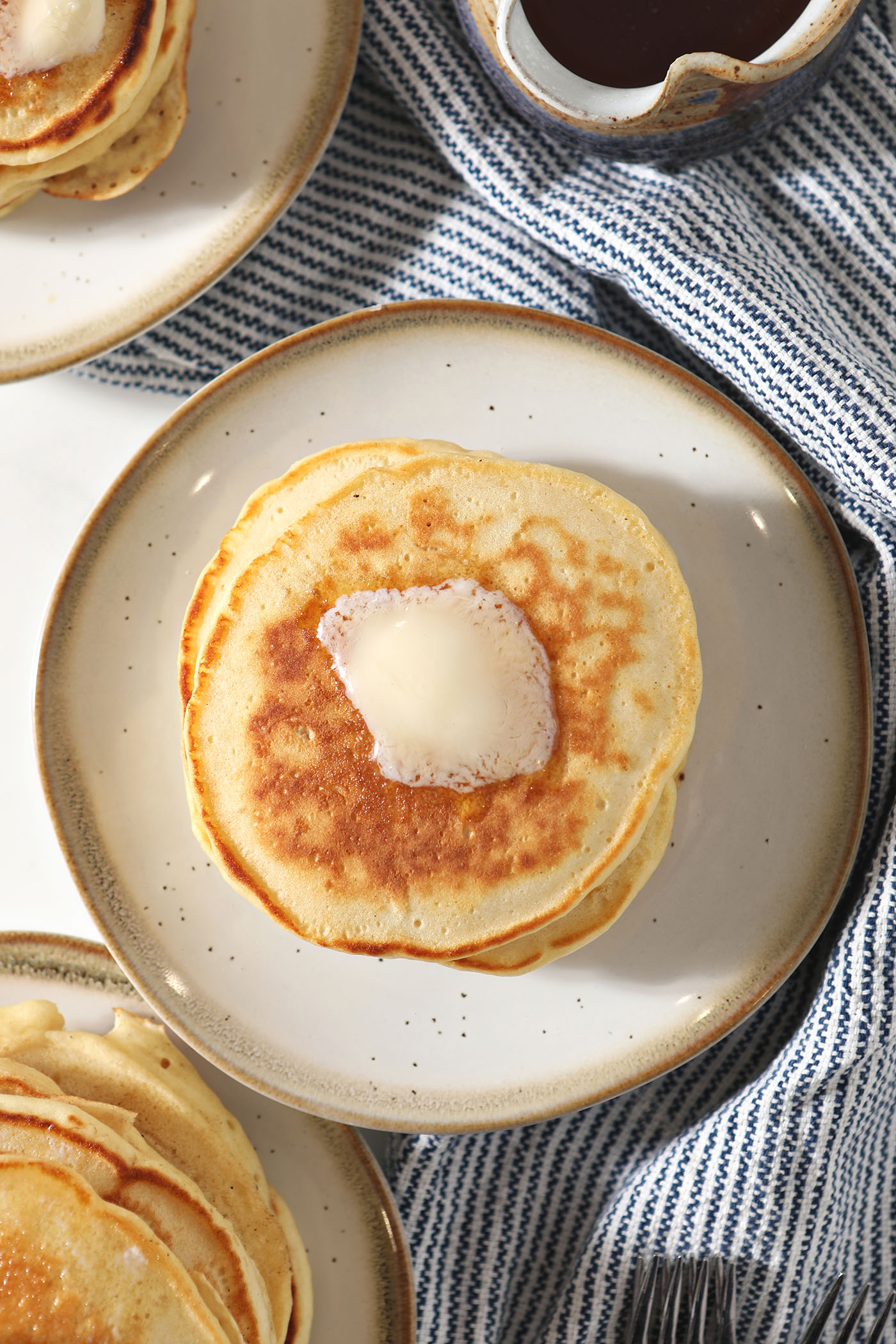 Overhead of a three plates holding stack of pancakes with butter on top of them
