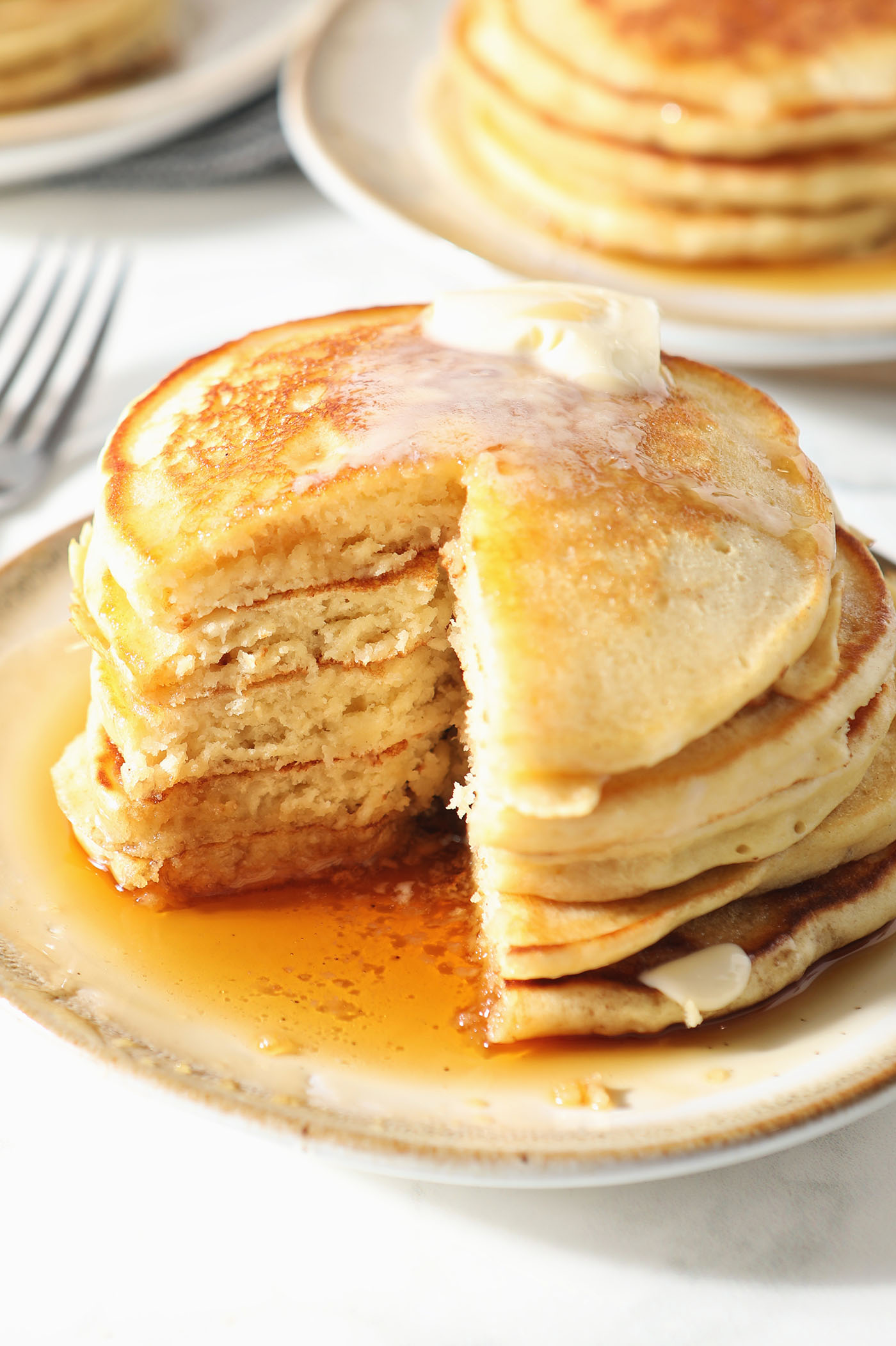 A cut-into stack of pancakes topped with melted butter and maple syrup on a plate on a marble surface