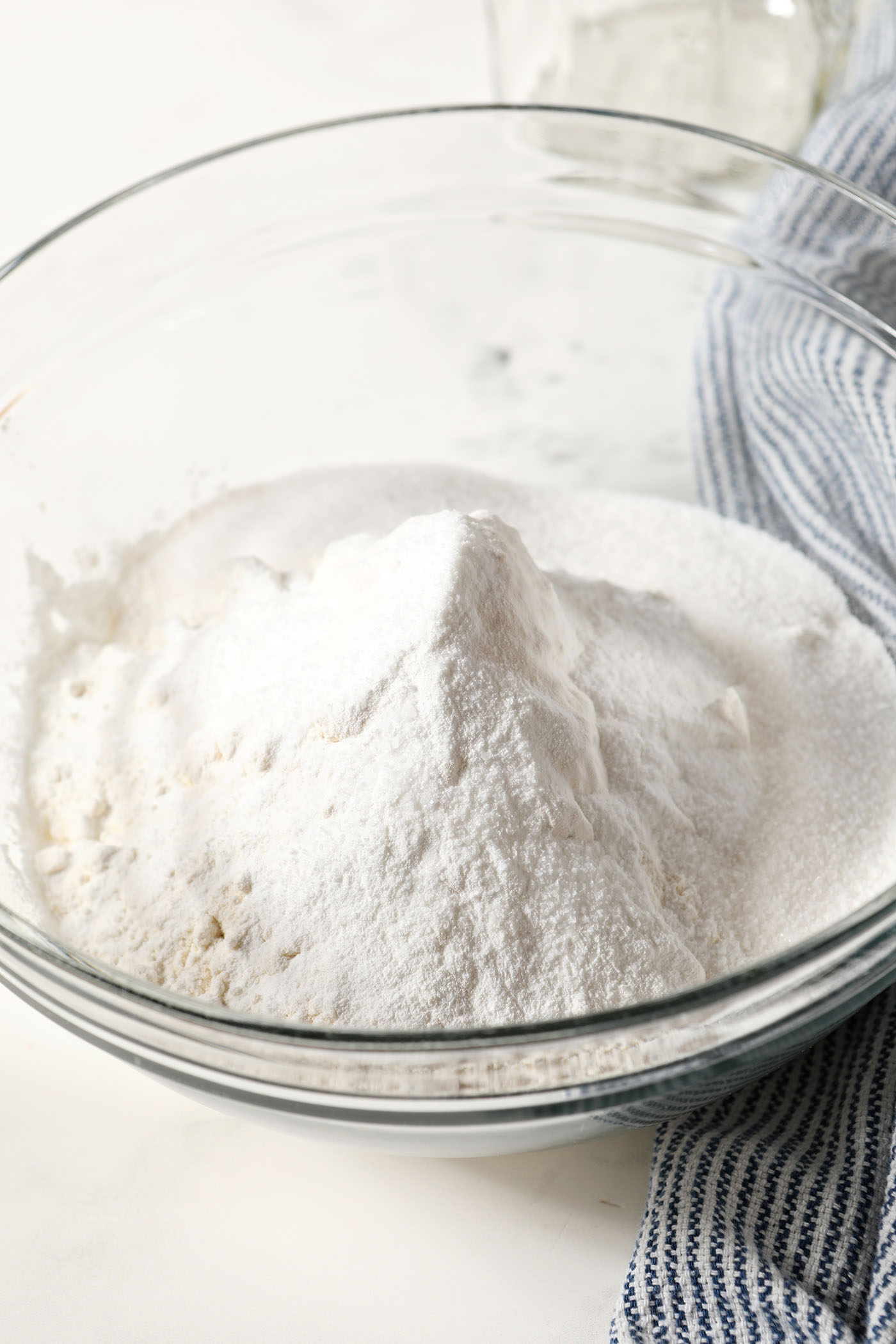 Dry ingredients in a bowl, before mixing, on a marble surface next to a blue and white striped linen