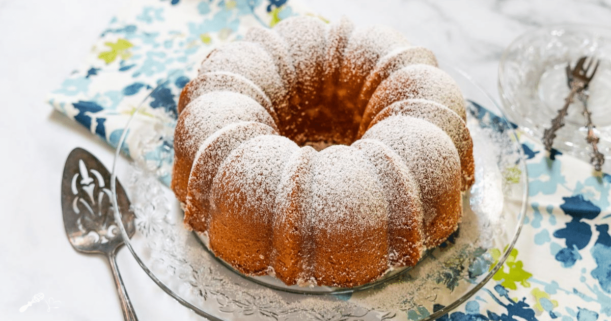 a bundt cake on a decorative plate covered in powdered sugar before slicing
