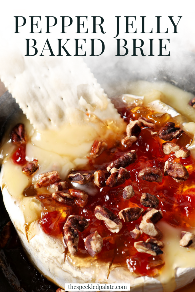 A cracker dips into gooey pepper jelly baked brie in a skillet next to baguette slices with the text pepper jelly baked brie