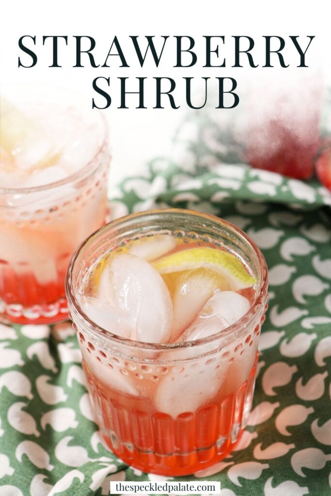 Two glasses of strawberry shrub, garnished with lemon wedges, on a green patterned linen, with the text strawberry shrub