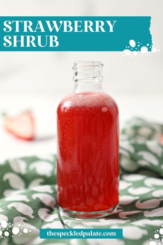 A bottle of homemade strawberry shrub syrup on a green patterned linen with the text strawberry shrub