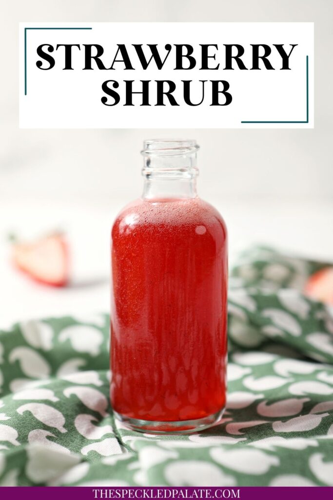 A bottle of homemade strawberry shrub syrup on a green patterned linen with the text strawberry shrub