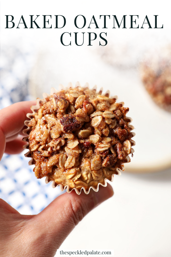 A hand holds an oatmeal muffin cup in hand above a plate with two more and a blue patterned linen