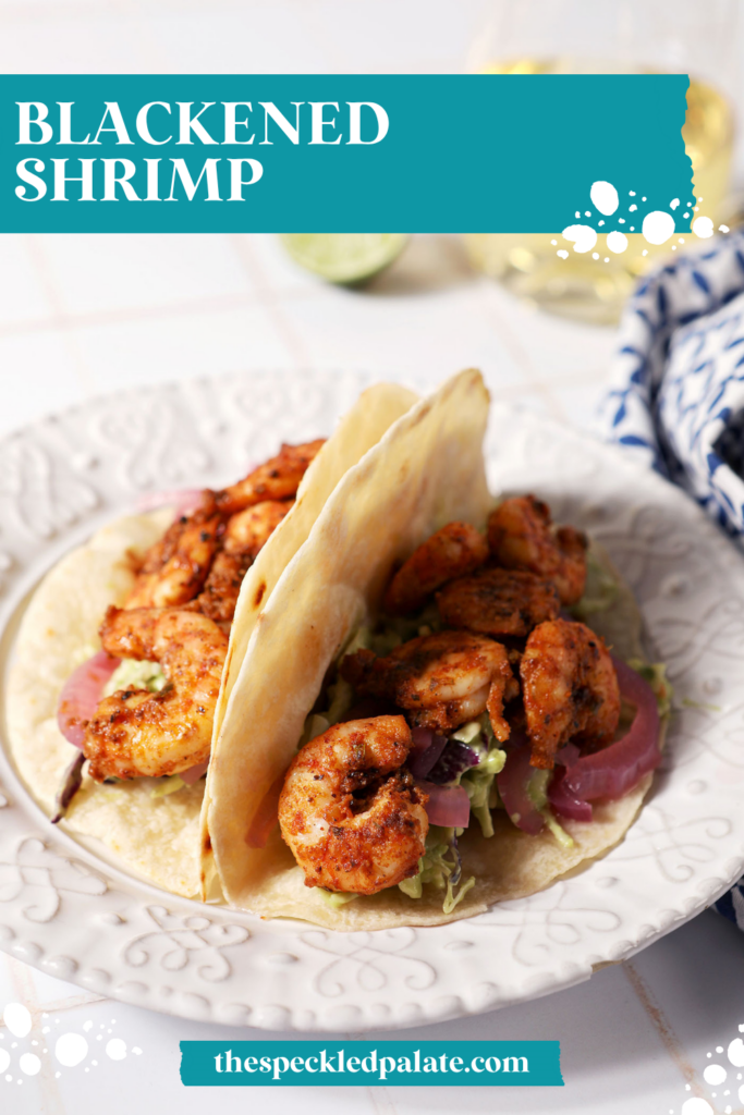 Two blackened shrimp tacos on a white plate on a white tiled surface