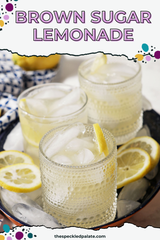 Four glasses of brown sugar lemonade on a blue tray with ice cubes and lemon wheels on a marble surface, next to a blue patterned linen, more lemon slices, and a bowl of brown sugar with the text "Brown Sugar Lemonade" on top.