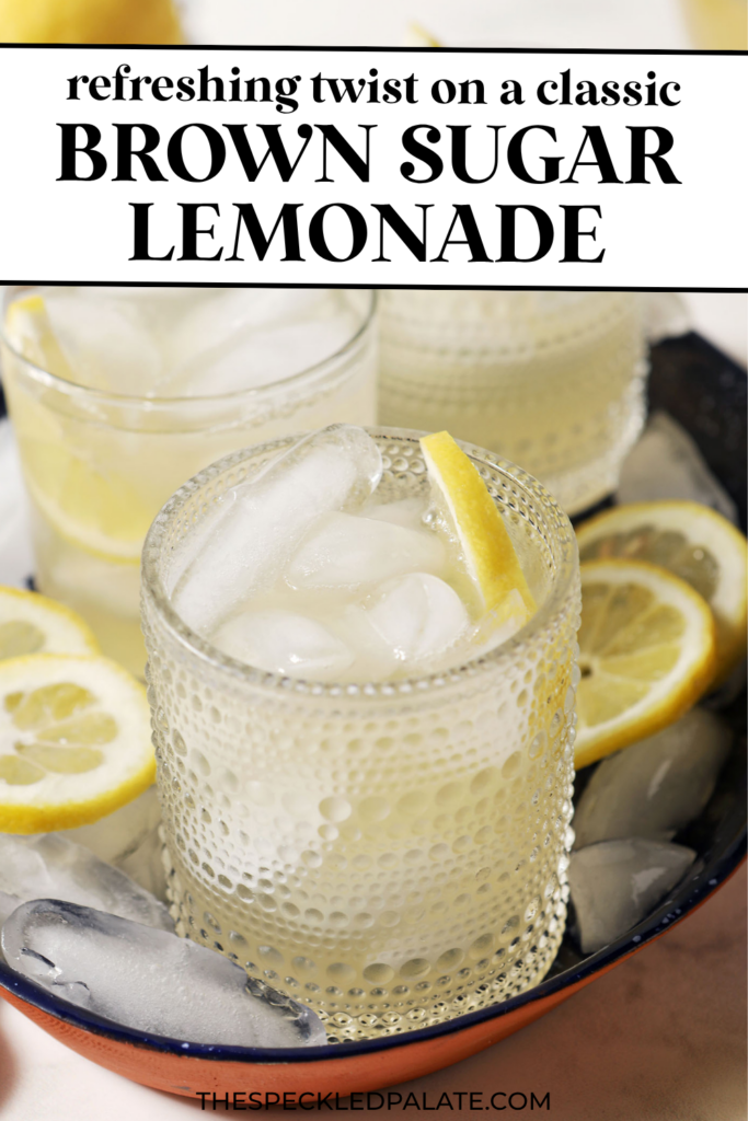 Four glasses of brown sugar lemonade on a blue tray with ice cubes and lemon wheels on a marble surface, next to a blue patterned linen, more lemon slices, and a bowl of brown sugar with the text "Brown Sugar Lemonade" on top.