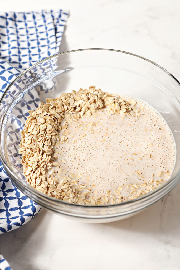 Oatmeal in a bowl with liquid, before mixing, on a marble surface with a blue patterned linen