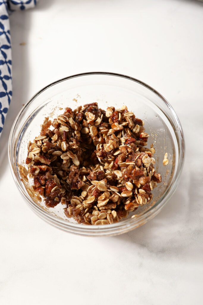 Pecan crumble topping in a bowl on a marble surface next to a blue patterned linen