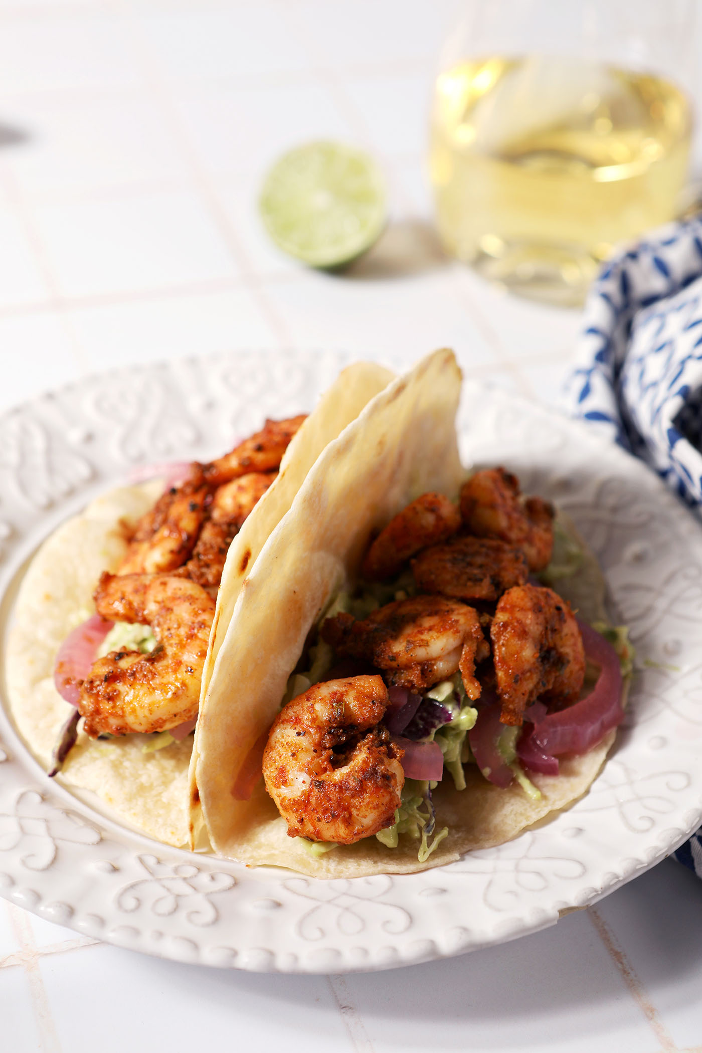 Two blackened shrimp tacos on a white plate on a white tiled surface