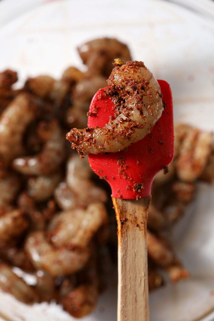 Seasoned shrimp before cooking on a red spatula