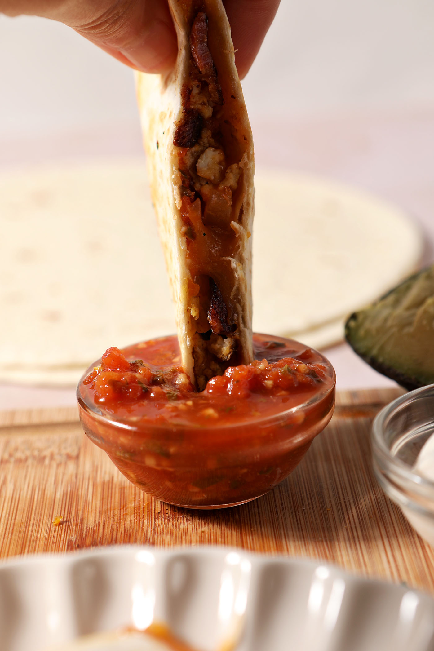 A breakfast quesadilla dips into a bowl of salsa.
