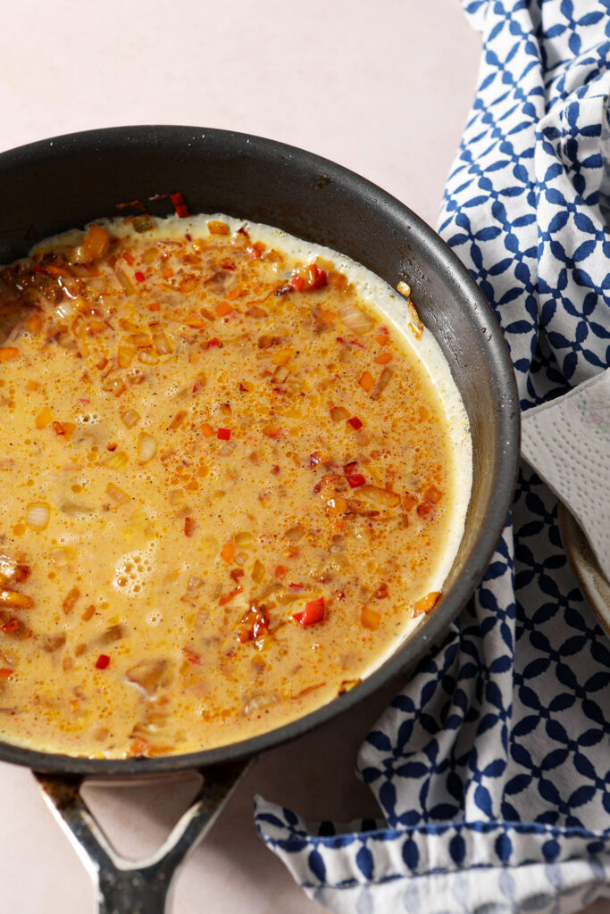 Eggs sit on top of diced vegetables before scrambling