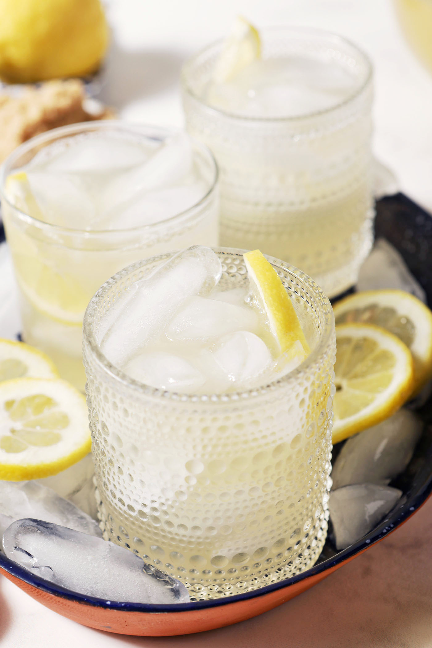 Three lemonades sit on a blue tray surrounded by ice cubes and sliced lemons