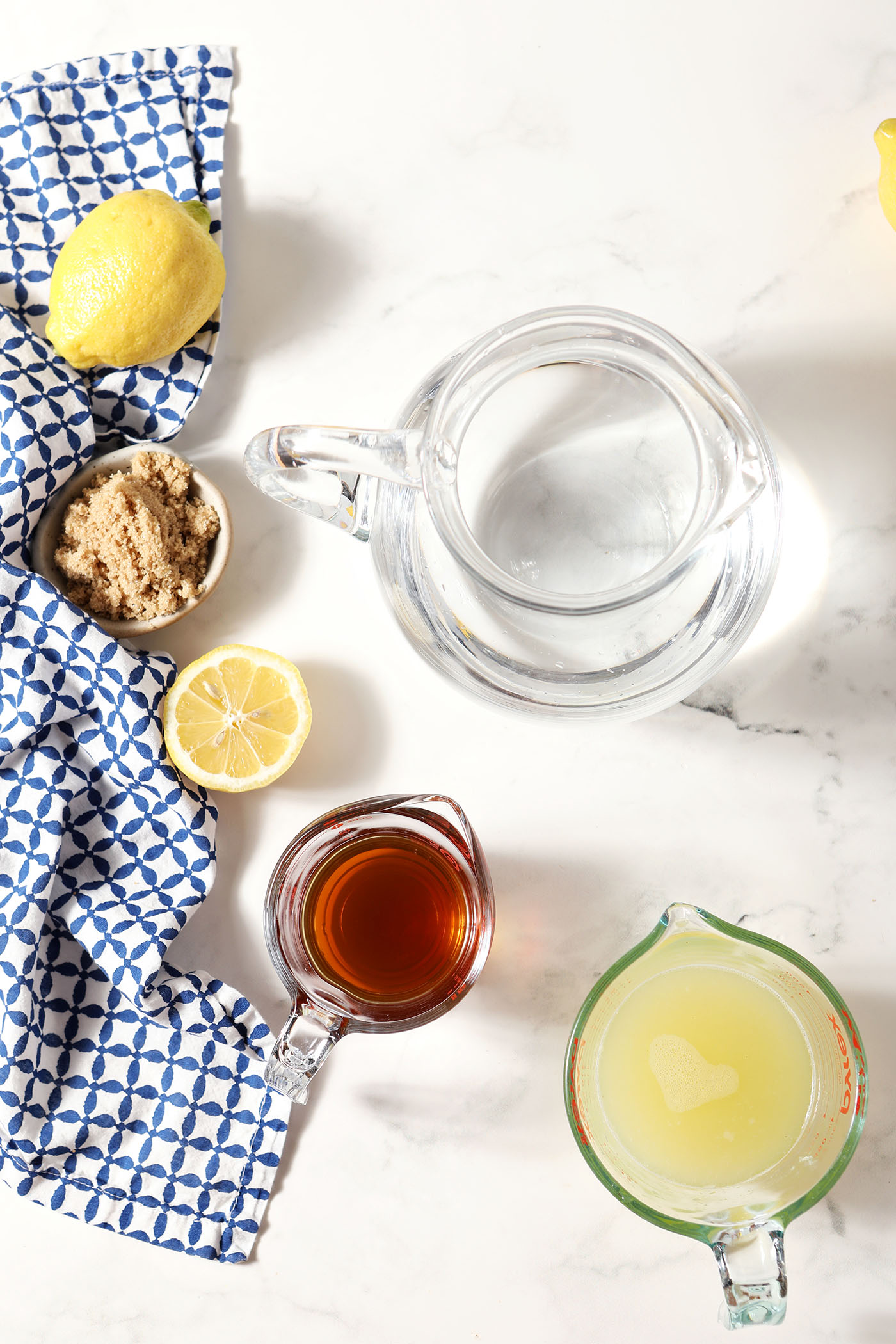Ingredients to make brown sugar lemonade with a brown sugar syrup on a marble surface next to a blue patterned linen