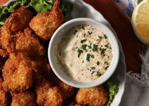 A remoulade in a bowl next to fried shrimp
