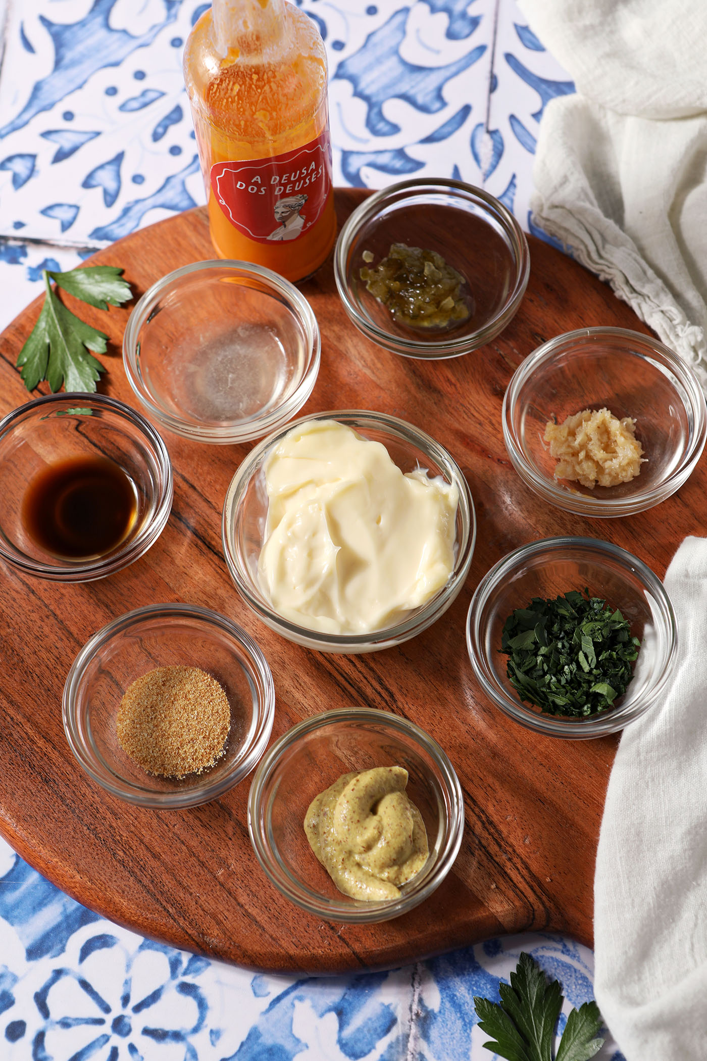 Ingredients to make a Remoulade sauce in bowls on a wooden board on top of a blue and white tile surface