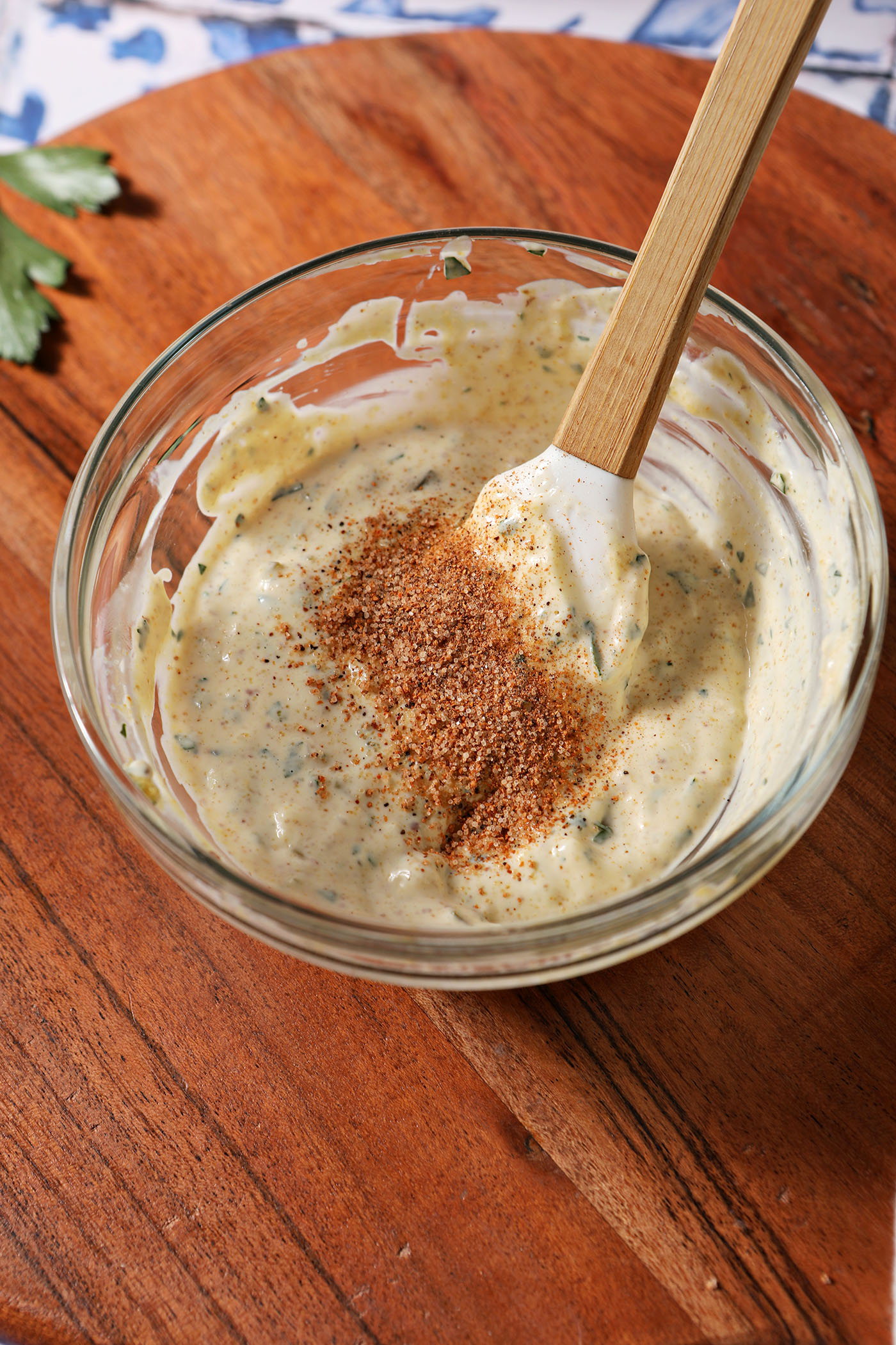 A Remoulade sauce in a bowl on a wooden surface with a rubber spatula inside it and Cajun seasoning on top.