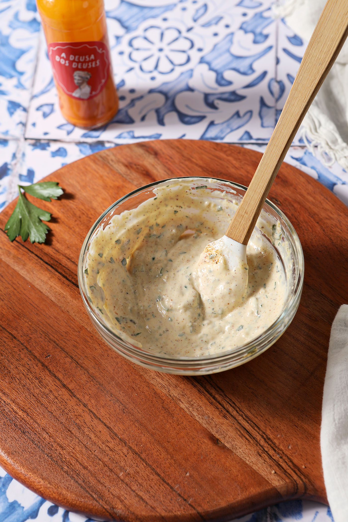 A bowl of Remoulade on a wooden surface in front of a bottle of Portuguese hot sauce.