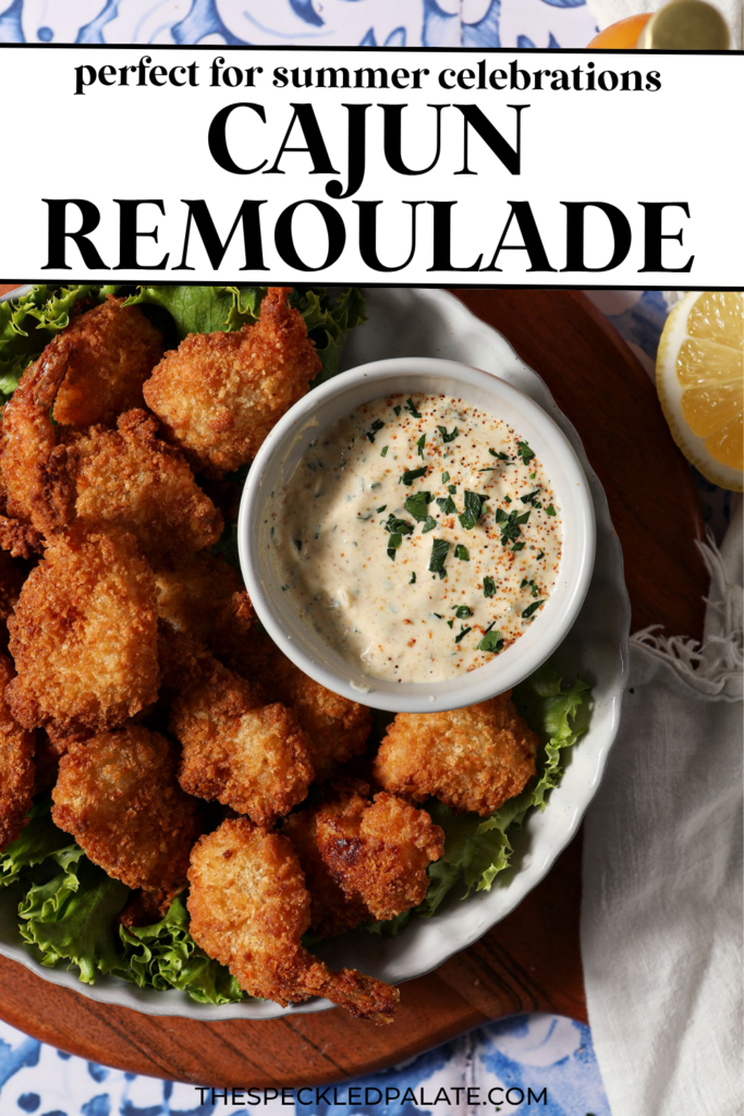 A bowl of Cajun Remoulade sauce sits on a platter with fried shrimp and fresh lettuce on top of a wooden platter on a blue and white tile surface.