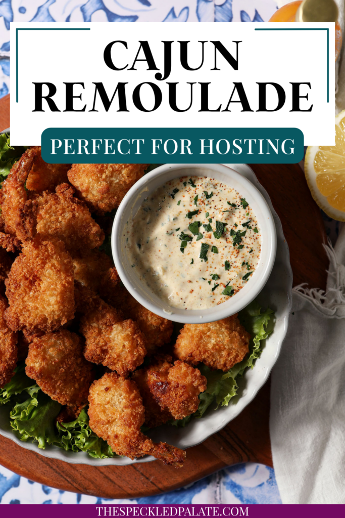 A bowl of Cajun Remoulade sauce sits on a platter with fried shrimp and fresh lettuce on top of a wooden platter on a blue and white tile surface.