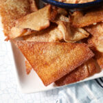 Closeup of a triangular wonton chip on a platter next to a dessert dip