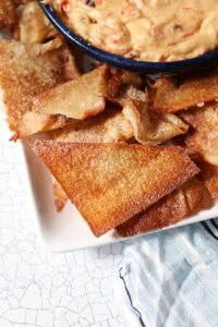 Closeup of a triangular wonton chip on a platter next to a dessert dip