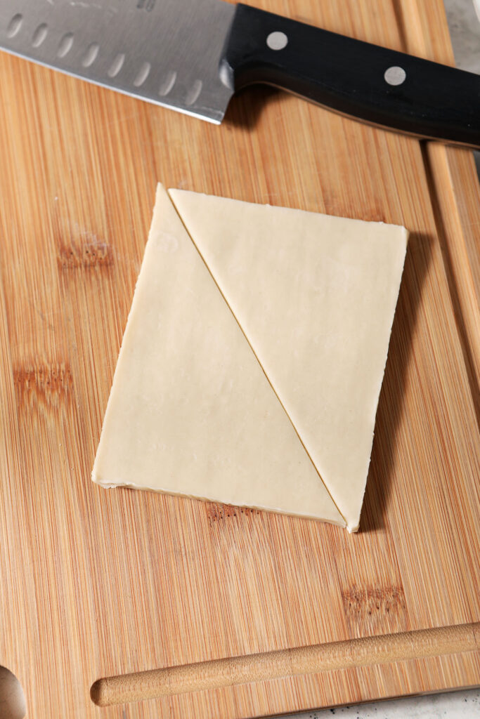 A stack of wontons on a wooden cutting board, halved, sitting next to a knife