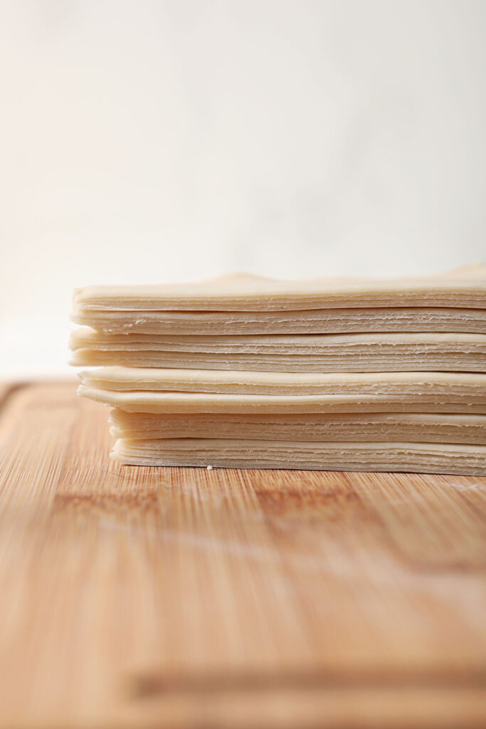 A stack of halved wonton wrappers on a wooden cutting board
