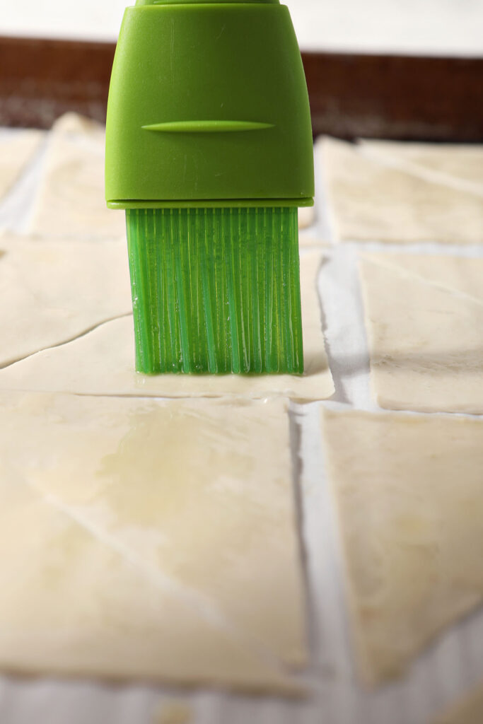A green pastry brush brushes butter onto wontons