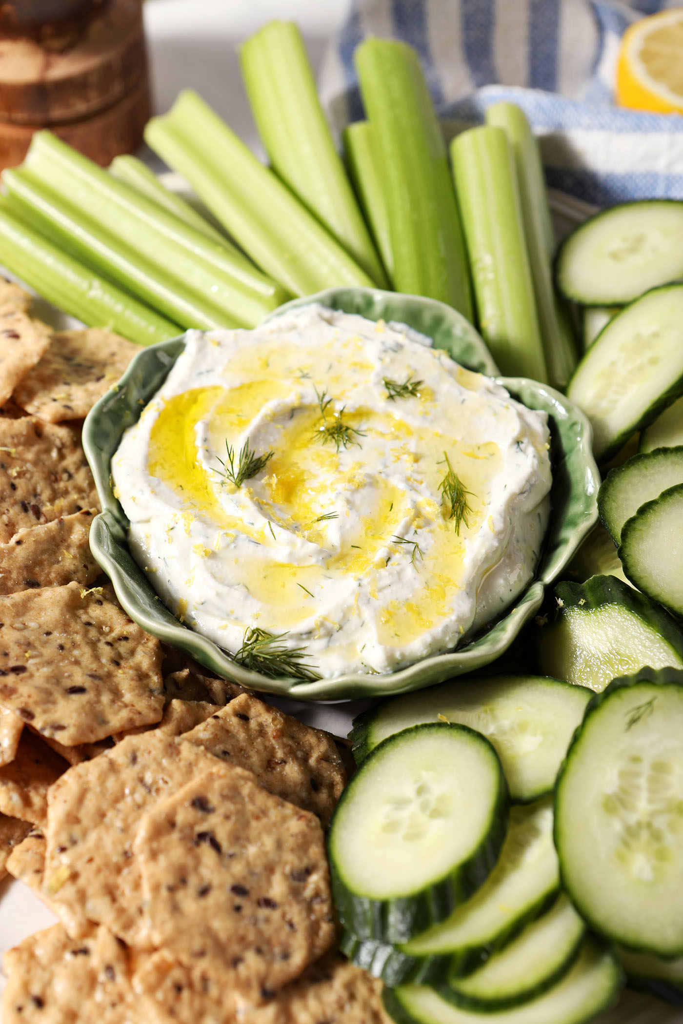 Creamy cottage cheese dip, garnished with lemon zest, olive oil and dill fronds, on a platter with chips, celery sticks and cucumber rounds