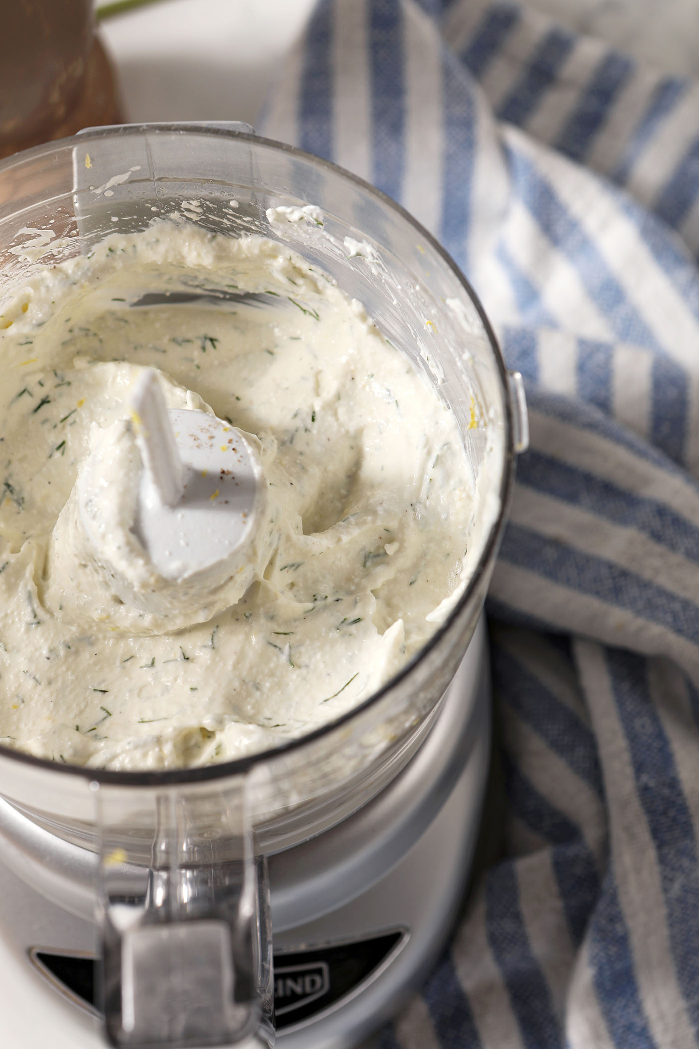Blended cottage cheese dip in a food processor next to a blue and white striped linen