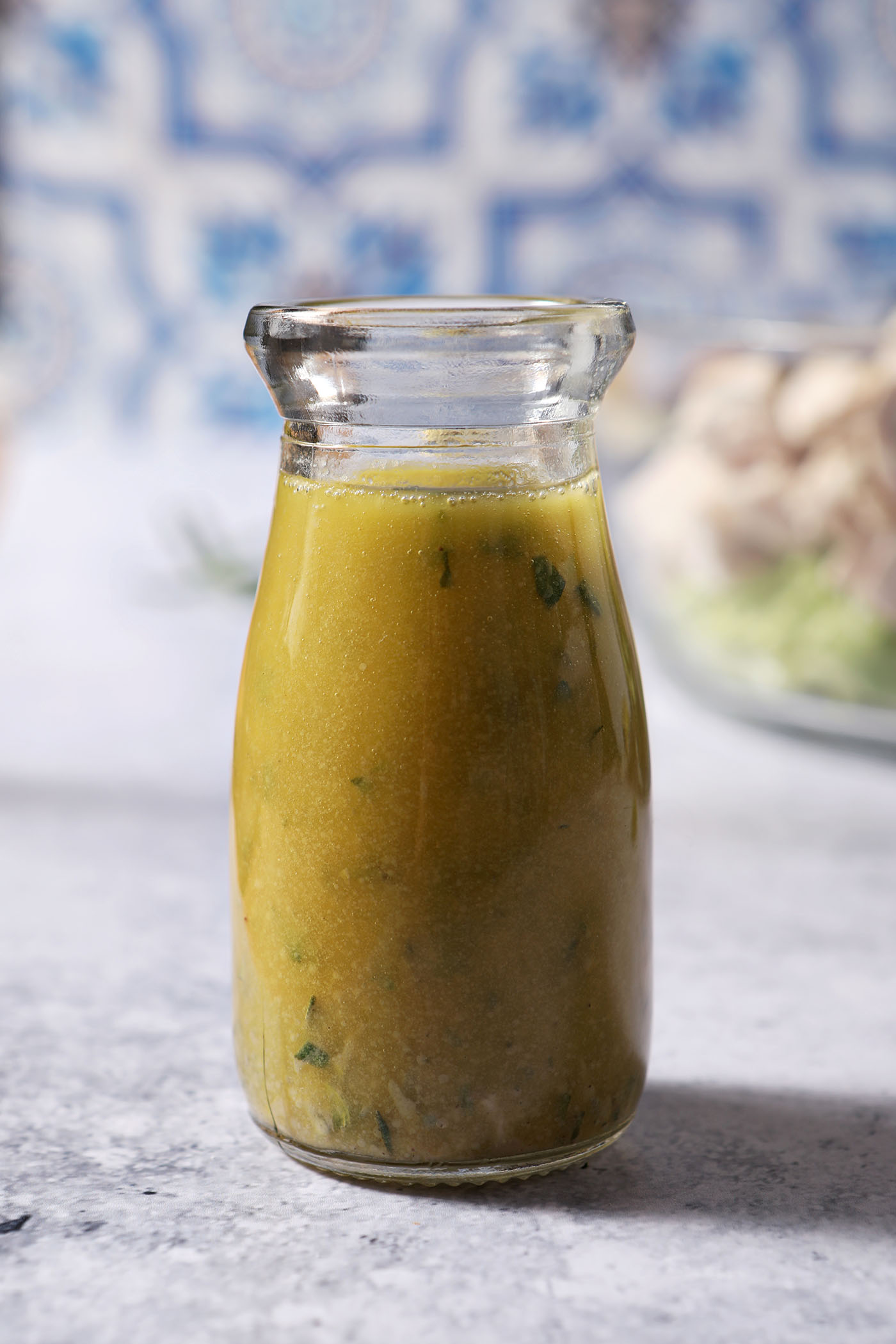 A bottle of lemon vinaigrette on a stone surface in front of a blue and white tiled backsplash