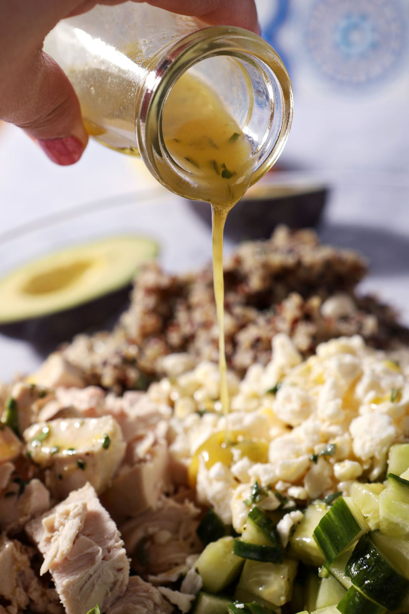 A bottle of lemon vinaigrette pours on top of salad ingredients in a bowl.