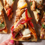 A hand grabs a slice of barbecue chicken flatbread from a platter