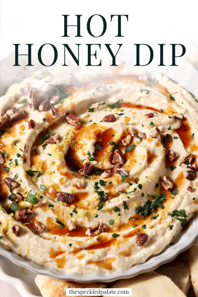 Hot honey dip, garnished with more hot honey, chopped pecans, chopped herbs and lemon zest, in a gray bowl with fresh pita