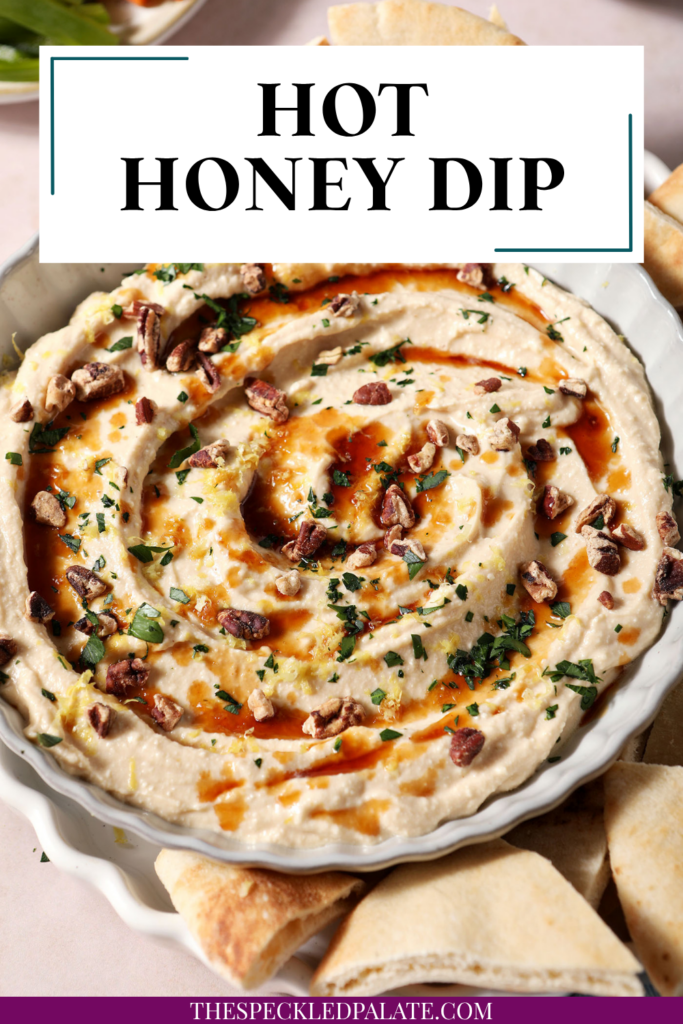 Hot honey dip, garnished with more hot honey, chopped pecans, chopped herbs and lemon zest, in a gray bowl with fresh pita