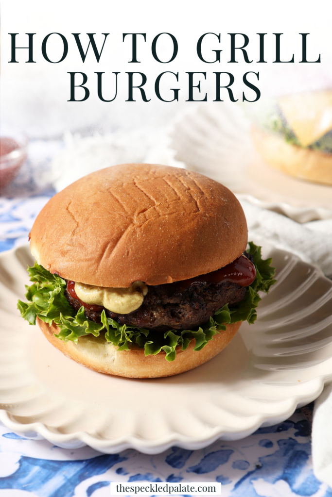 A dressed grilled hamburger sits on a plate on a blue tiled surface.