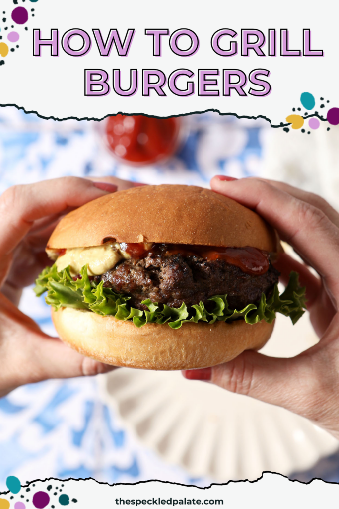 A woman holds a grilled burger in her hands above a blue and white tiled surface with plates, fries, and ketchup.