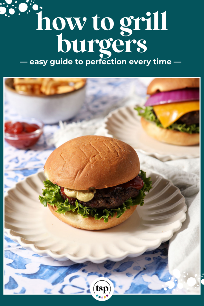 A dressed grilled hamburger sits on a plate on a blue tiled surface.