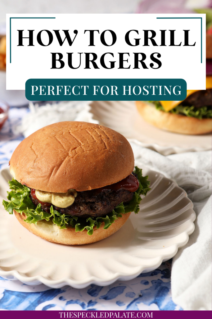 A dressed grilled hamburger sits on a plate on a blue tiled surface.